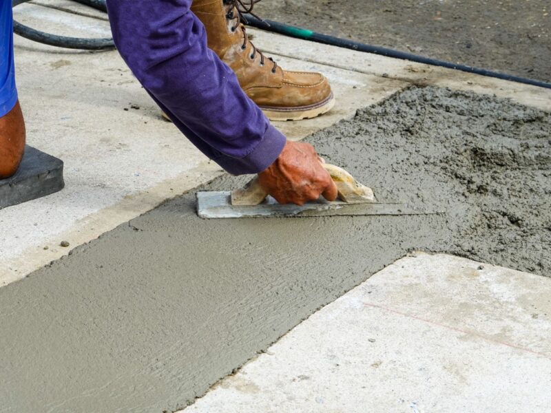 Worker smoothing out wet concrete flooring. 