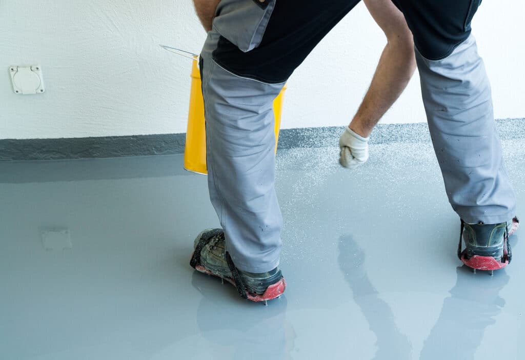 A construction worker renovates balcony floor and spreads watertight resin and glue before chipping and sealing