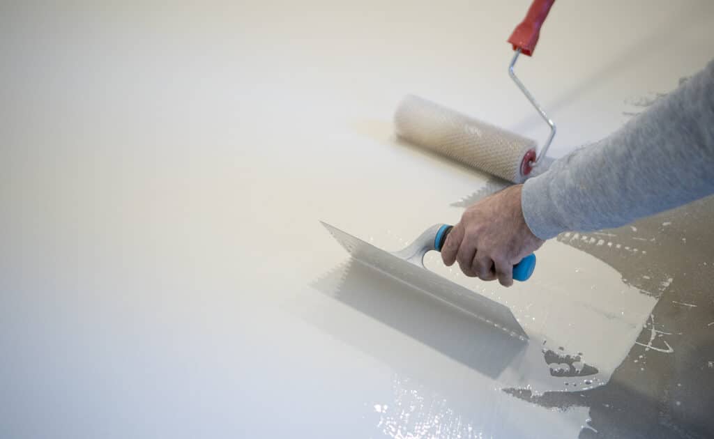 worker painting white polyurethane resin on concrete floor